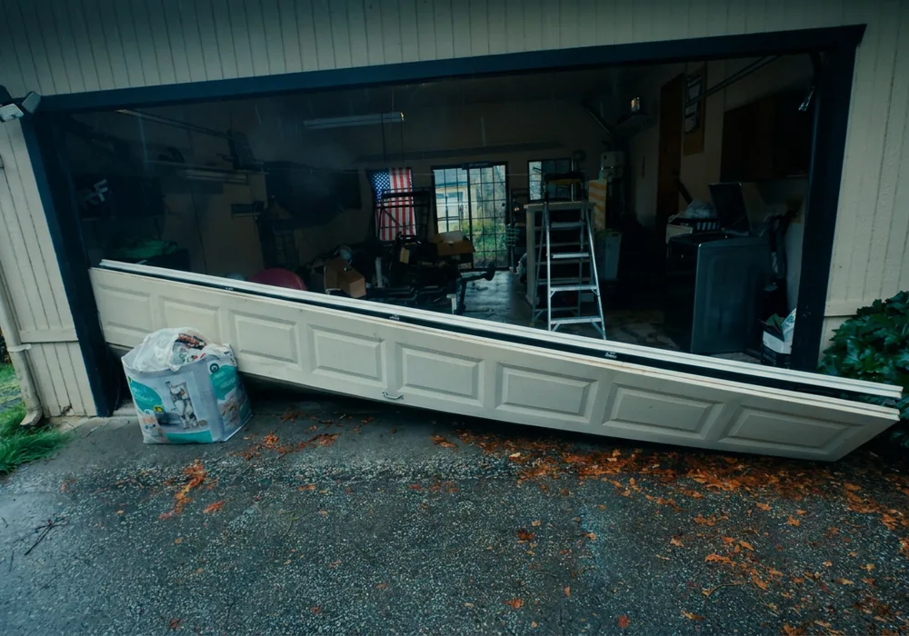 Garage door section lifted out of its tracks and leaning into the driveway